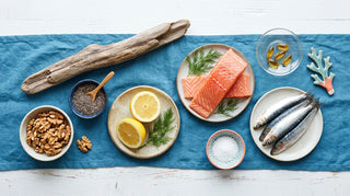 Coastal flat lay of omega-3 fish oil sources with salmon, sardines, walnuts, chia, lemon, and amber softgels