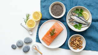 Flat lay of salmon, sardines, walnuts, chia seeds, and lemon on a white and ocean-blue surface