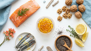 Flat lay of whole-food omega-3 sources and amber softgels on a bright white surface