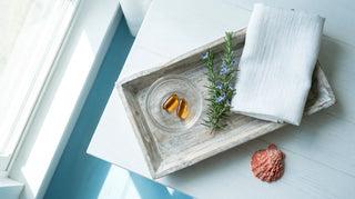 Premium amber omega-3 softgels in a glass dish on a coastal-styled flat lay arrangement