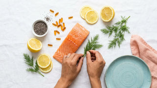 Flat lay hero image of omega-3 rich foods and amber softgels arranged on a white linen backdrop with coastal accents