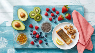 Flat lay of omega-3 rich fruits, salmon, walnuts, chia seeds, and amber softgels on an ocean-blue themed surface