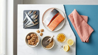 Overhead flat lay of salmon, sardines, walnuts, chia seeds and amber omega-3 softgels on a white and blue surface