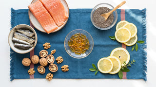 Flat lay of amber omega-3 softgels with salmon, walnuts, chia, and lemon on a white surface