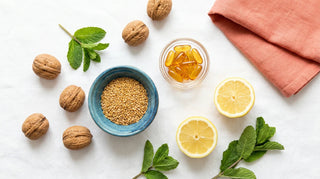 Flat lay of walnuts, flaxseeds, amber omega-3 softgels, and lemon on a bright white surface