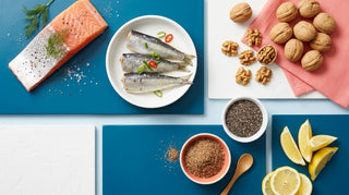 Flat lay of omega-3 foods including salmon, sardines, walnuts, chia, and flaxseed on an ocean-blue surface